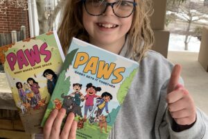 Smiling girl holding up two books in the PAWS series and giving a thumbs-up sign
