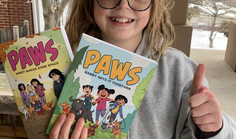 Smiling girl holding up two books in the PAWS series and giving a thumbs-up sign